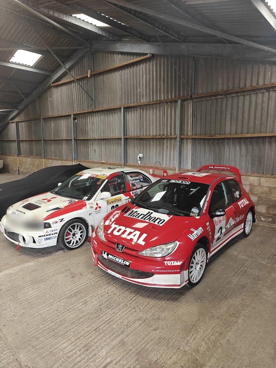 The Peugeot 206 WRC and Mitsubishi Evo IV parked together in the garage
